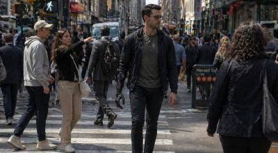 Homme avec main robotique augmentée marchant dans une rue fréquentée de New York pendant que des passants observent la prothèse mécanique